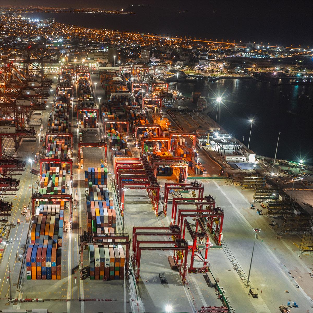 uber-uns.feat Beleuchteter Containerhafen bei Nacht mit Kränen, Containern und Logistikbetrieb in voller Auslastung.
